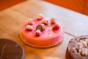 Okrągły różowy torcik ozdobiony malinami i cukrem.