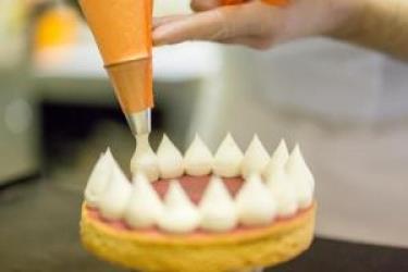 Dekorowanie ciasta bitą śmietaną za pomocą rękawa cukierniczego.