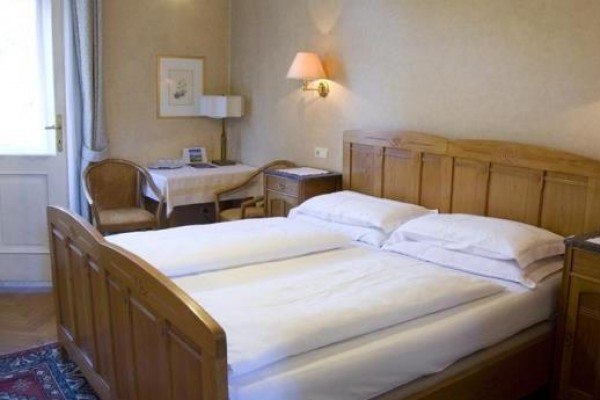Pokój hotelowy z drewnianym łóżkiem, stolikiem nocnym i małym stołem z dwoma krzesłami.