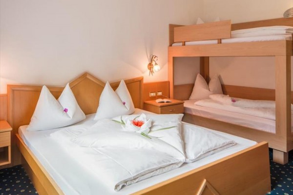 Pokój hotelowy z podwójnym łóżkiem i łóżkiem piętrowym, pościel zdobiona kwiatami.