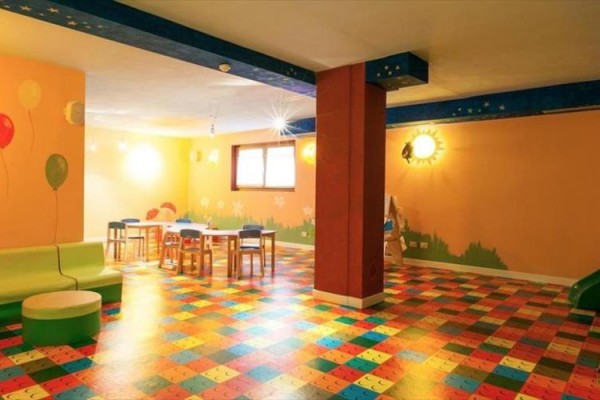 Sala zabaw z kolorową podłogą i ściennymi motywami balonów i krajobrazu.