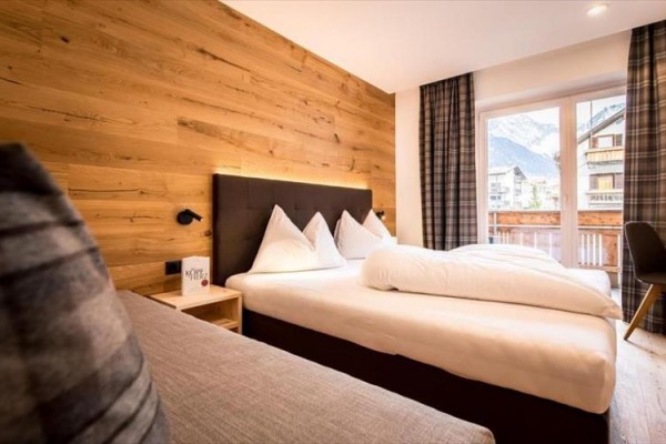 Nowoczesny pokój hotelowy z drewnianą ścianą, dużym łóżkiem i widokiem na góry.