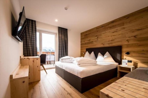 Nowoczesny pokój hotelowy z drewnianymi meblami, łóżkiem małżeńskim i balkonem z widokiem na zewnątrz.