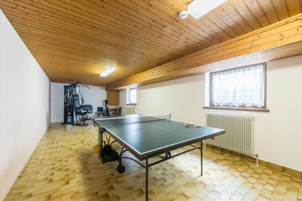 Pomieszczenie z sufitem z drewnianych desek zawierające stół do tenisa stołowego i atlas do ćwiczeń.