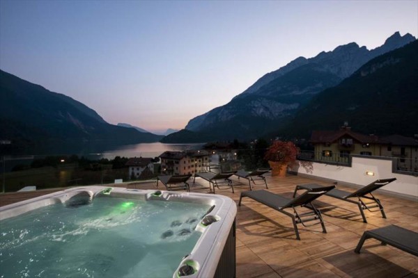 Jacuzzi na tarasie z widokiem na jezioro i górski krajobraz o zmierzchu.