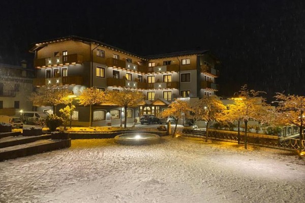 Nocą zasypany śniegiem budynek hotelu z oświetlonymi drzewami i fontanną.