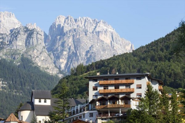 Hotel z drewnianymi balkonami u podnóża zalesionej góry ze skalistymi szczytami.