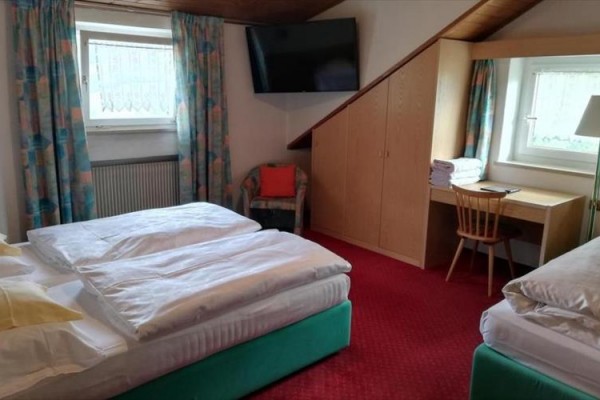 Pokój hotelowy z dwoma łóżkami, telewizorem i biurkiem pod skośnym sufitem.
