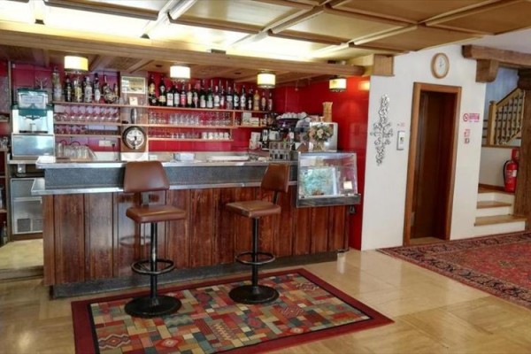 Bar z drewnianym blatem, dwoma krzesłami i wyeksponowanymi butelkami napojów.