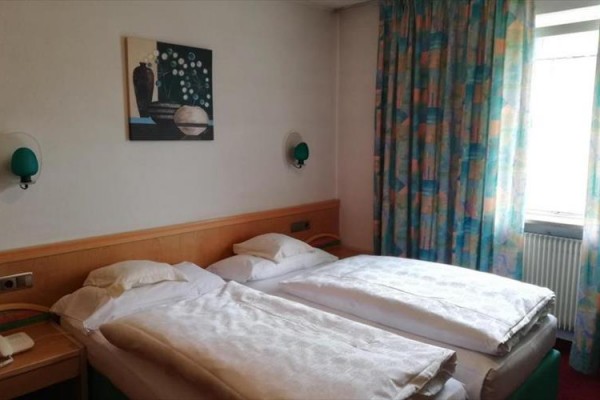 Dwa jednoosobowe łóżka w pokoju hotelowym z obrazem na ścianie i kolorowymi zasłonami przy oknie.