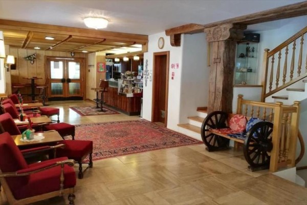 Hol hotelowy z czerwonymi fotelami, dywanem i drewnianymi schodami.
