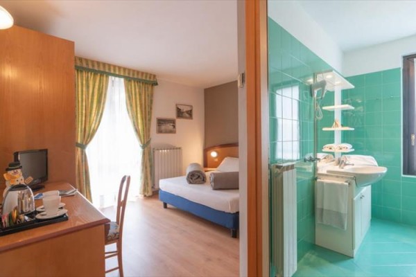 Pokój hotelowy z łóżkiem małżeńskim i otwartą łazienką z zielonymi kafelkami.