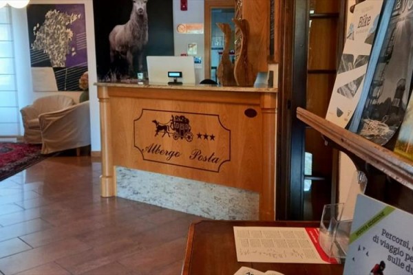 Recepcja hotelu Albergo Posta z oznaczeniem trzech gwiazdek i materiałami reklamowymi na pierwszym planie.