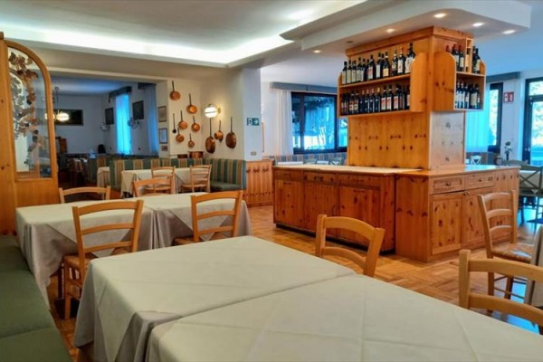 Restauracja z drewnianymi meblami i butelkami wina na półce za barem.