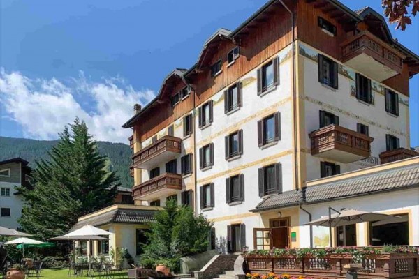 Czteropiętrowy hotel z drewnianymi balkonami otoczony zielenią.