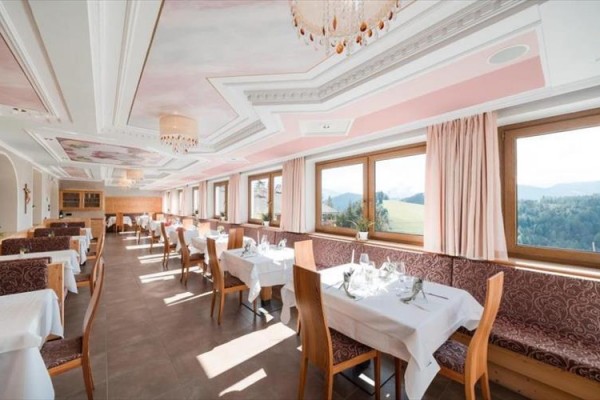 Jasna restauracja z dużymi oknami z widokiem na krajobraz, nakryte stoły i krzesła z jasnego drewna.