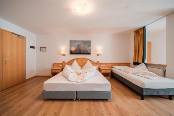 Pokój hotelowy z podwójnym łóżkiem, jasnymi drewnianymi meblami i pościelą złożoną w kształt kwiatu.