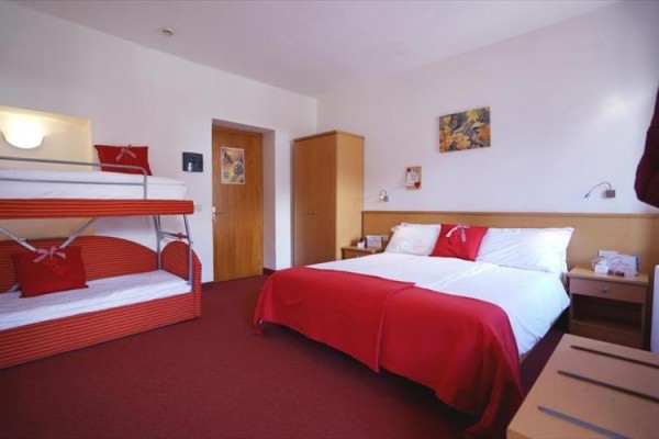 Pokój hotelowy z łóżkiem małżeńskim i łóżkiem piętrowym, utrzymany w czerwonych tonacjach.
