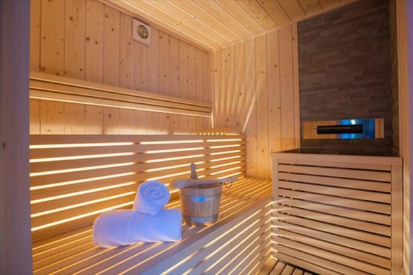 Drewniana sauna z ławką, ręcznikiem i wiadrem w środku.