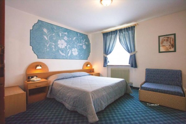 W pokoju znajdują się łóżko, stoliki nocne, niebieska sofa i zasłony przy oknie.