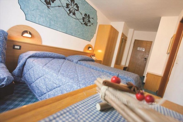 Dwa pojedyncze łóżka z niebieską narzutą w hotelowym pokoju z drewnianymi meblami.