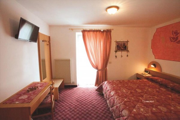 Pokój hotelowy z podwójnym łóżkiem, zasłoną i telewizorem na ścianie.