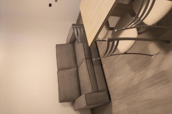 Szara sofa obok jasnego drewnianego stołu i dwóch krzeseł.