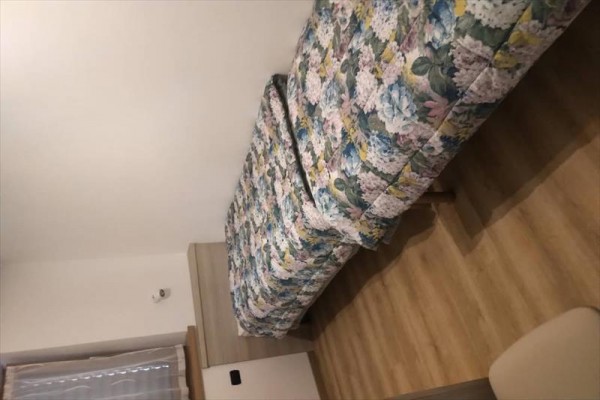 Pojedyncze łóżko z wzorzystą narzutą w pokoju z drewnianą podłogą.