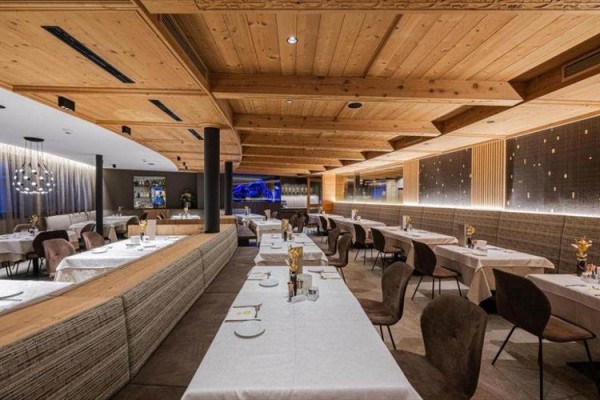 Elegancka restauracja z drewnianym sufitem i stołami z białymi obrusami.