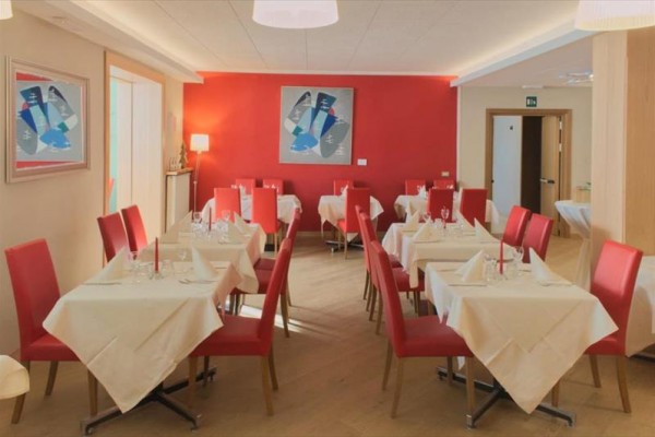 Restauracja z czerwonymi krzesłami i białymi obrusami na stołach.