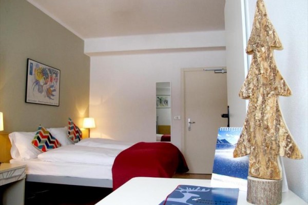 Nowoczesny pokój hotelowy z łóżkiem, dekoracyjnym drzewkiem i obrazkiem na ścianie.