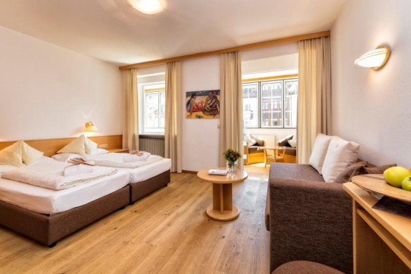 Jasny pokój hotelowy z dwoma łóżkami, kanapą, stołem i dużymi oknami.