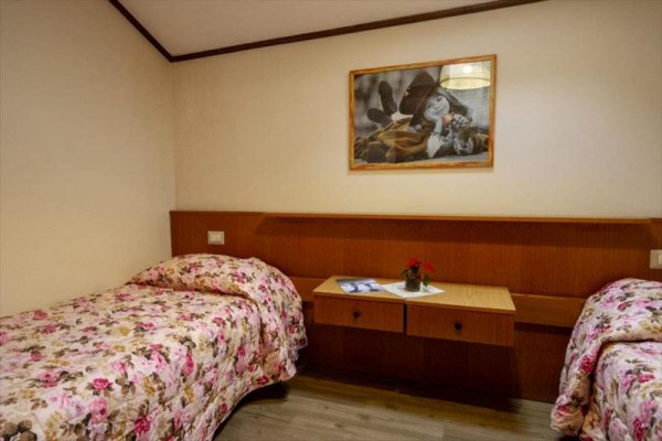 Pokój z dwoma osobnymi łóżkami z kwiecistymi narzutami, stolikiem nocnym i obrazem na ścianie.