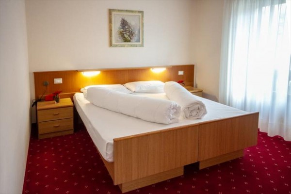 Łóżko dwuosobowe z białą pościelą w pokoju hotelowym z czerwonym dywanem.