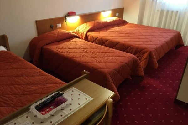 Trzy łóżka z czerwonymi narzutami w pokoju hotelowym.