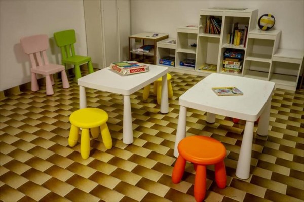 Dziecięca sala zabaw z kolorowymi krzesełkami i stolikami na szachownicowej podłodze.