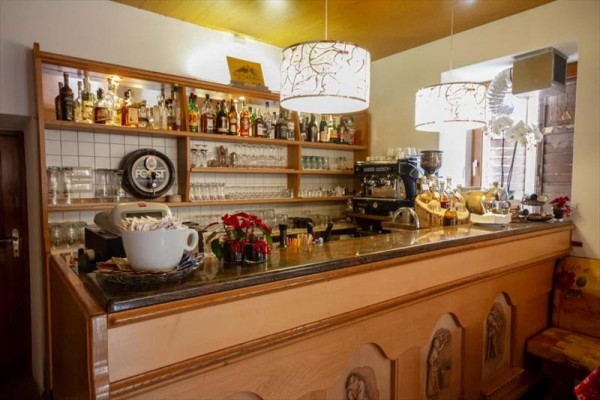 Bar z półkami pełnymi butelek alkoholu i szklankami obok ekspresu do kawy.