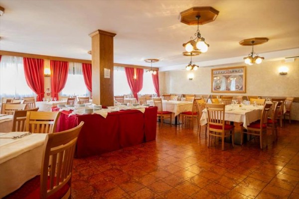 Restauracja z drewnianymi krzesłami, białymi obrusami i czerwonymi zasłonami.