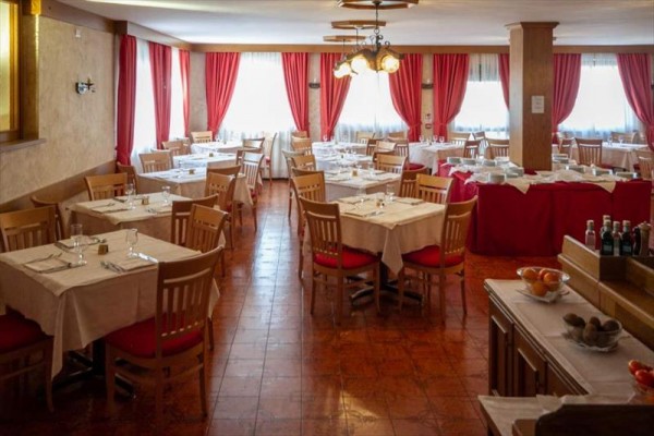 Wnętrze restauracji z drewnianymi stołami, krzesłami i czerwonymi zasłonami.