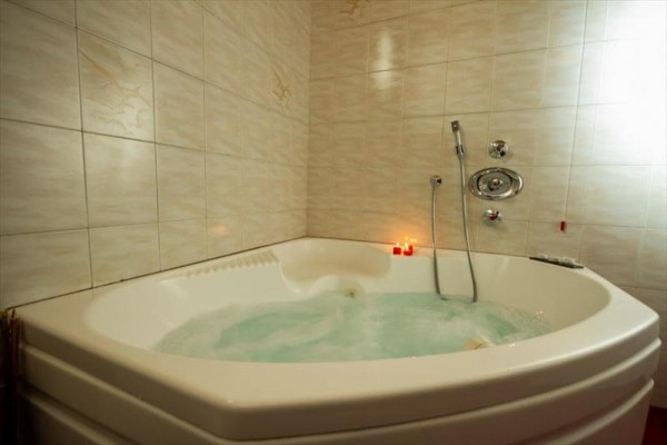 Wanna z hydromasażem w rogu łazienki z ceramicznymi płytkami i zapalonymi świecami.