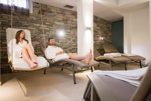 Dwie osoby relaksują się w szlafrokach na leżakach w pokoju z kamienną ścianą.