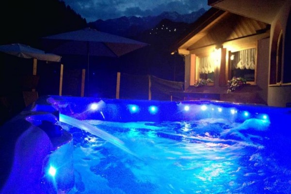 Jacuzzi z niebieskim oświetleniem w nocy obok domu.