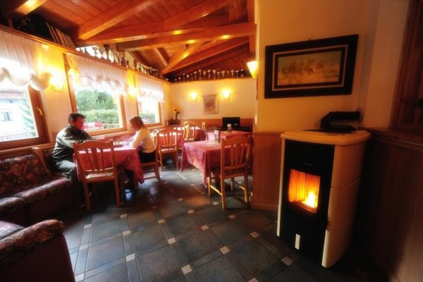 Przytulna restauracja z drewnianym sufitem, kominkiem i dwiema osobami siedzącymi przy stole przy oknie.