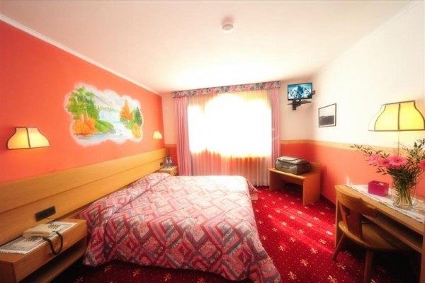 Pokój hotelowy w tonacji czerwieni i różu z podwójnym łóżkiem i telewizorem na ścianie.