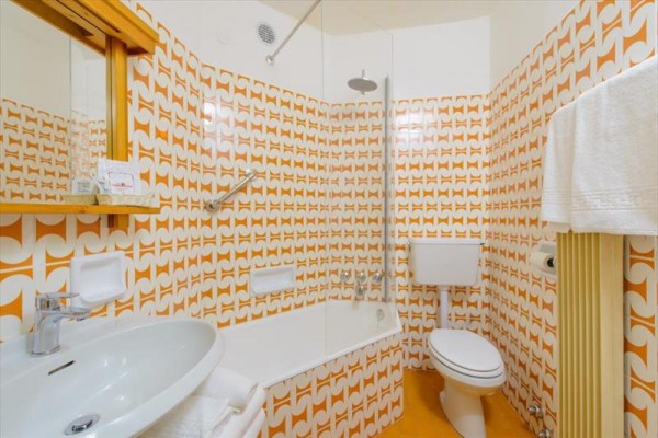 Łazienka z retro pomarańczowymi wzorzystymi płytkami, wanną i wiszącą toaletą.