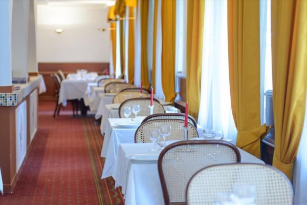 Restauracja z rzędami białych stołów z czerwonymi świecami i żółtymi zasłonami.