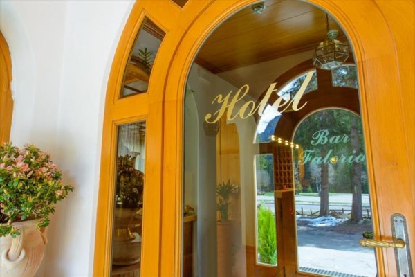 Szklane drzwi z napisami „Hotel” i „Bar Faloria” prowadzące do wnętrza budynku z łukowatymi drzwiami.