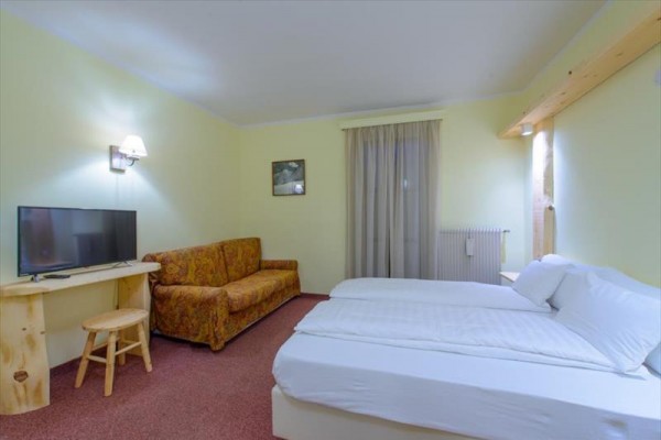 Jasny pokój hotelowy z dużym łóżkiem, kanapą i telewizorem na stoliku.