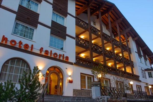 Fasada hotelu Faloria z drewnianym balkonem i oświetlonymi oknami o zmierzchu.