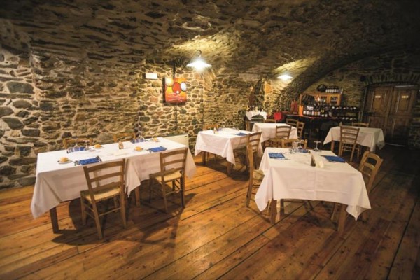 Restauracja z kamiennymi ścianami, drewnianą podłogą i kilkoma stolikami z białymi obrusami.